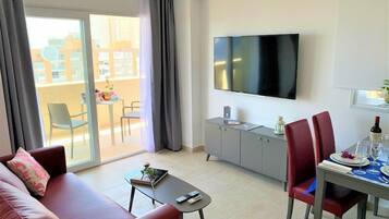 Un soggiorno moderno con divano, tavolino, tavolo da pranzo con sedie, TV a parete e balcone con tavolo e sedie.