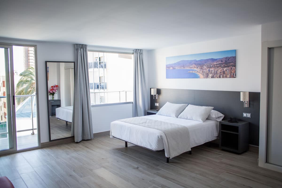 Una habitación de hotel moderna con una cama grande, una mesita de noche, un espejo y vistas de la ciudad a través de la ventana.