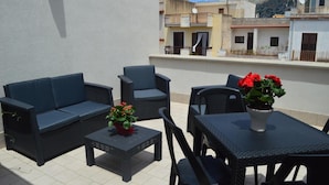 Un patio exterior con un sofá, sillas, una mesa y plantas en macetas.