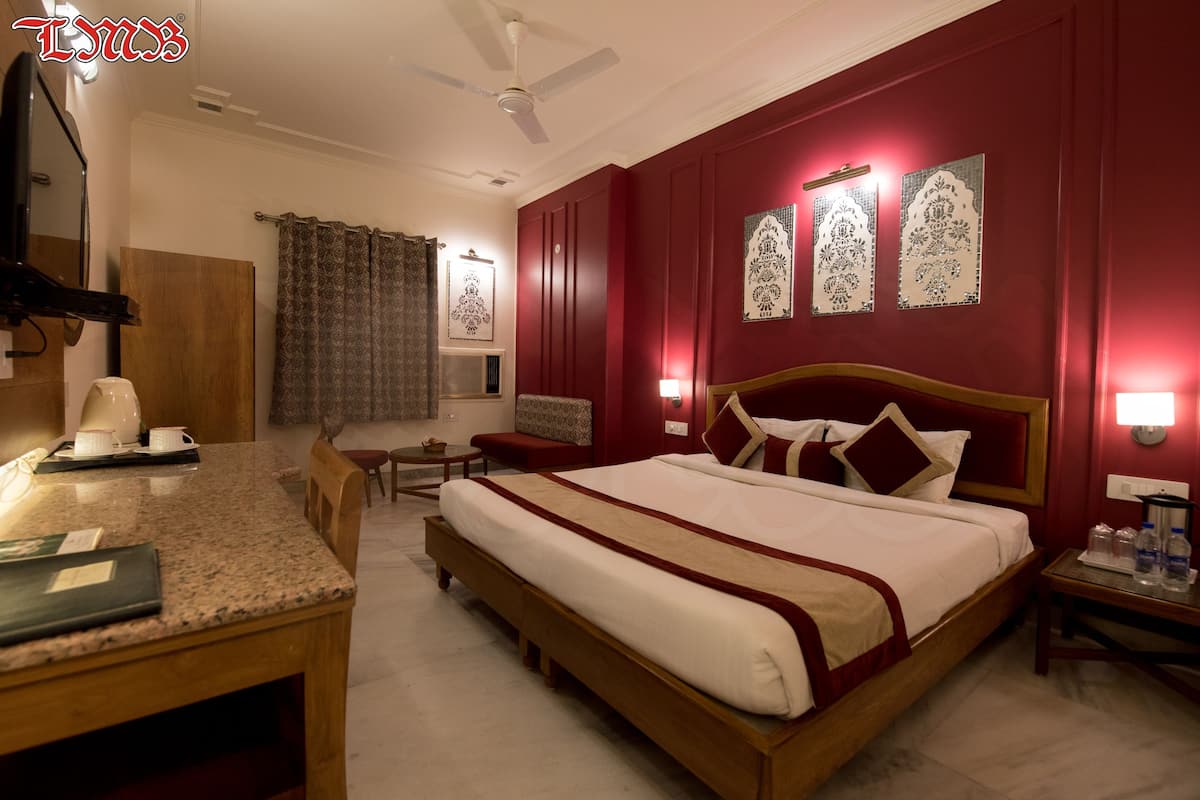 A hotel room with a large bed, a desk, a chair, a TV, and a ceiling fan.