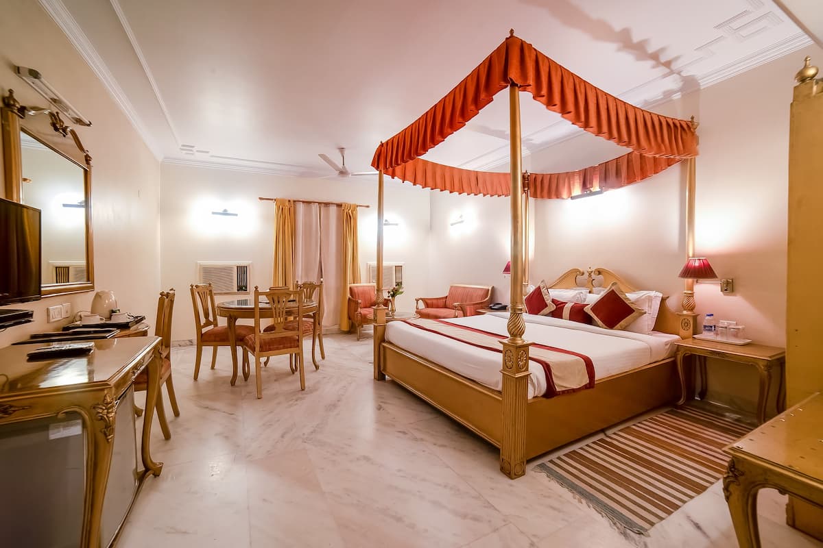 A four-poster bed with a canopy, a desk with a chair, a dining table with chairs, and a bedside table with a lamp.