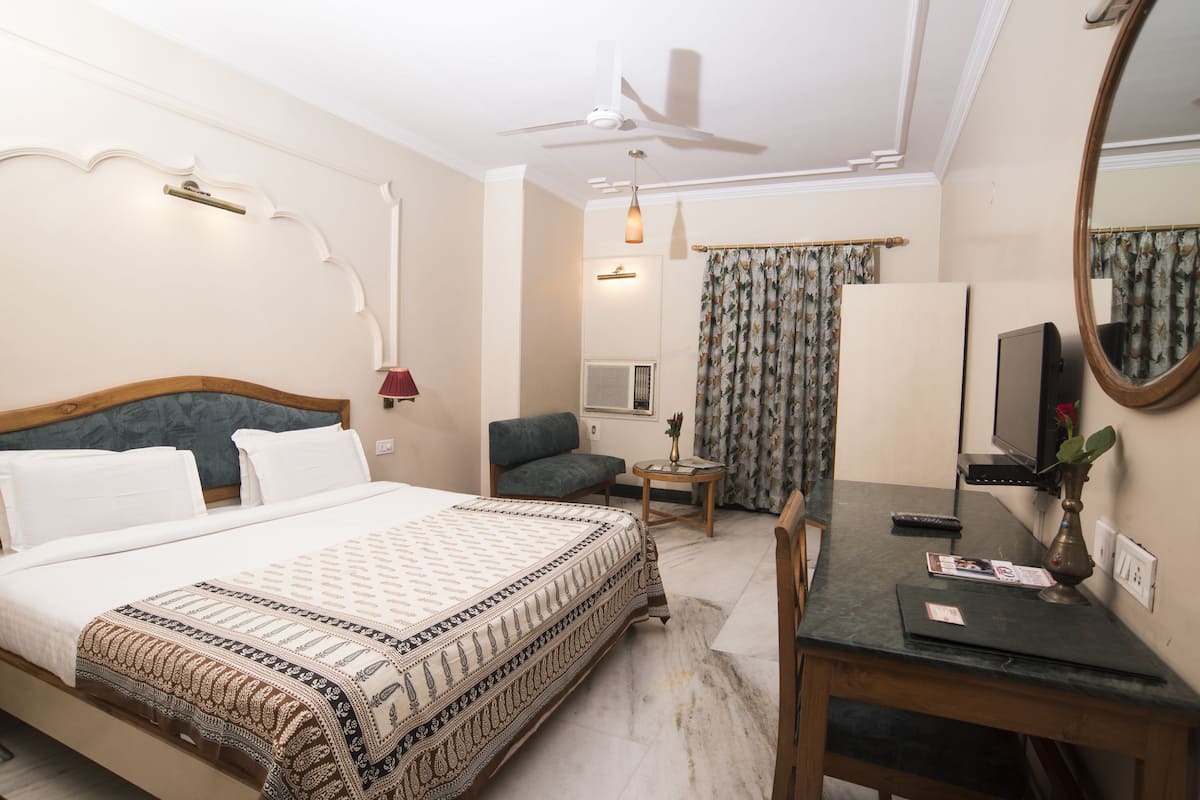 A hotel room with a bed, a desk, a chair, a television, and a ceiling fan.