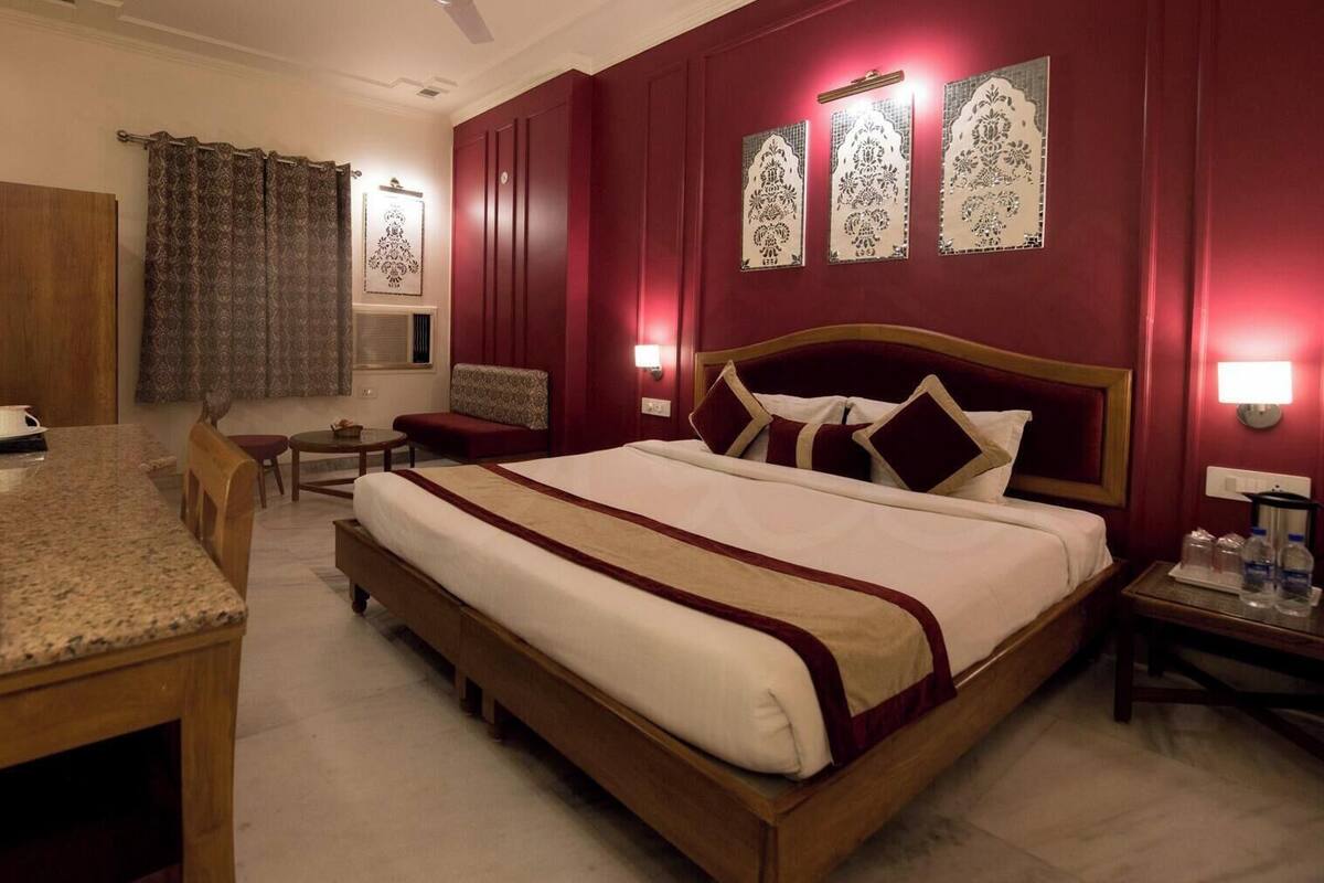 A hotel room with a bed, a desk, a chair, a small table, a mirror, and a window with curtains.