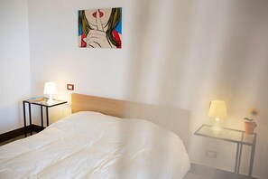 Habitación de hotel con una cama grande, dos mesitas de noche con lámparas, una obra de arte en la pared y una pequeña planta en maceta.