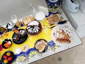 Een tafel gedekt met verschillende soorten eten, waaronder een taart, brood en gebak, op een betegelde vloer.