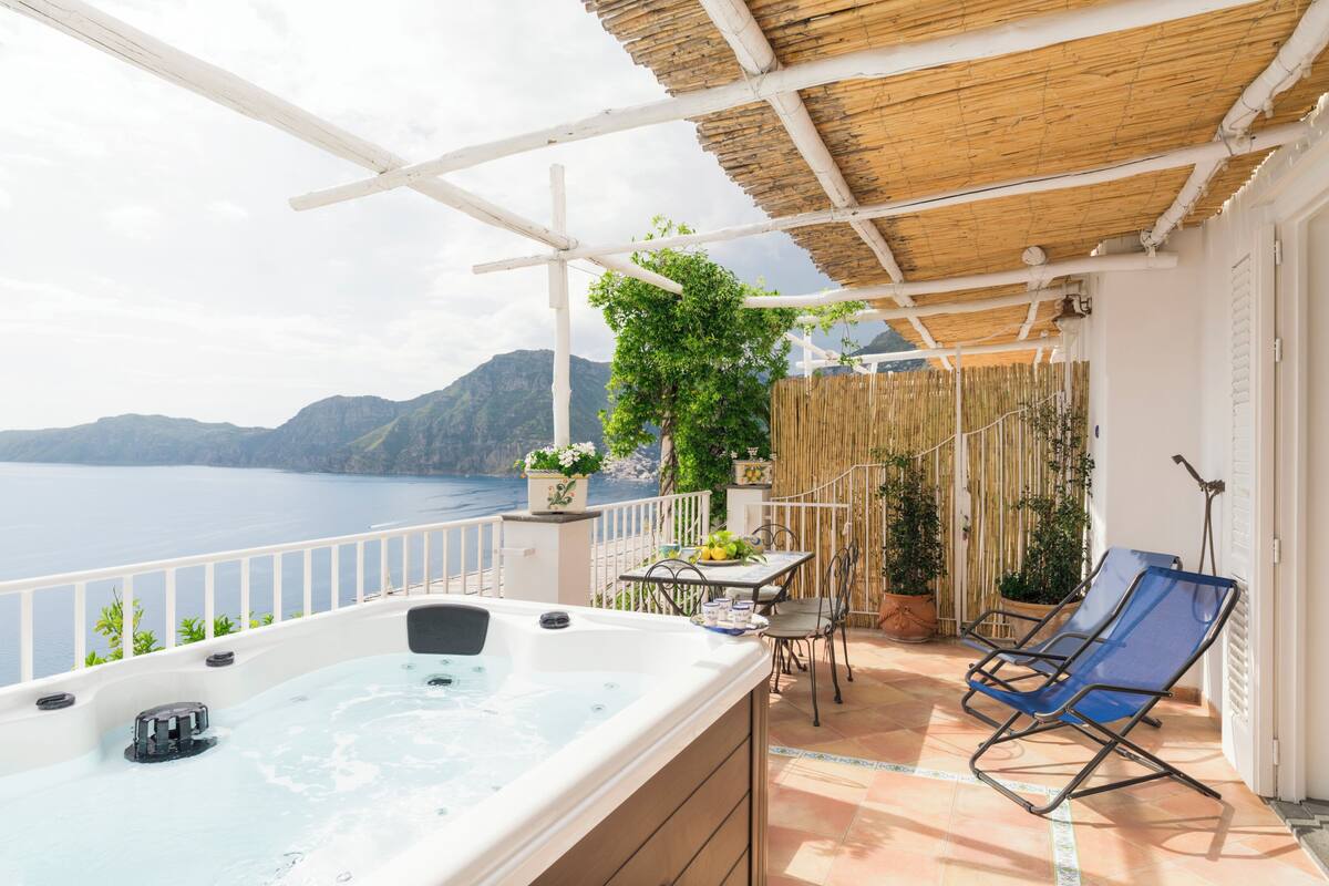 A balcony with a hot tub, a table with chairs, and potted plants.