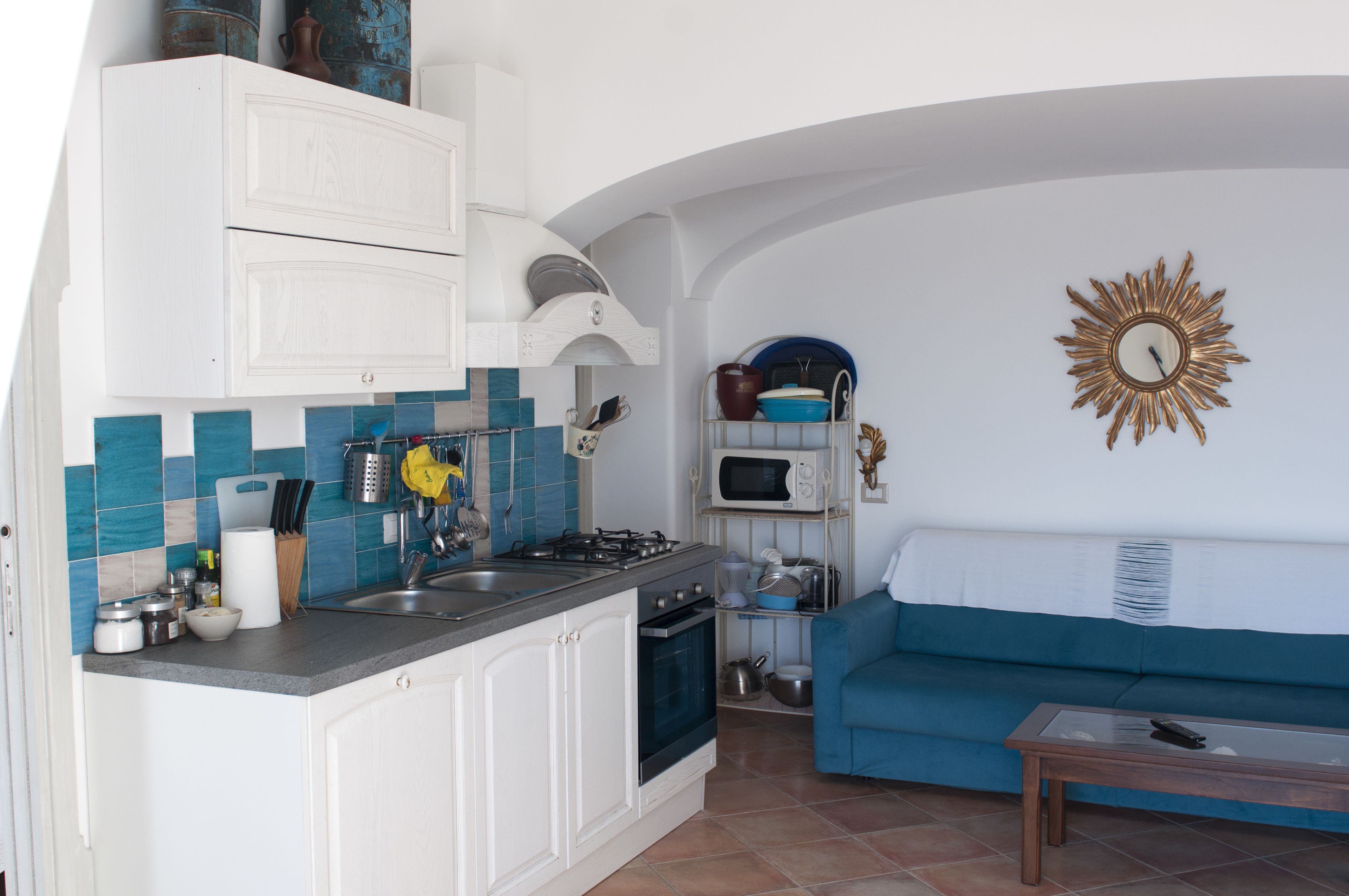 A compact kitchen with white cabinets, a blue tiled backsplash, and a blue sofa in the living area.