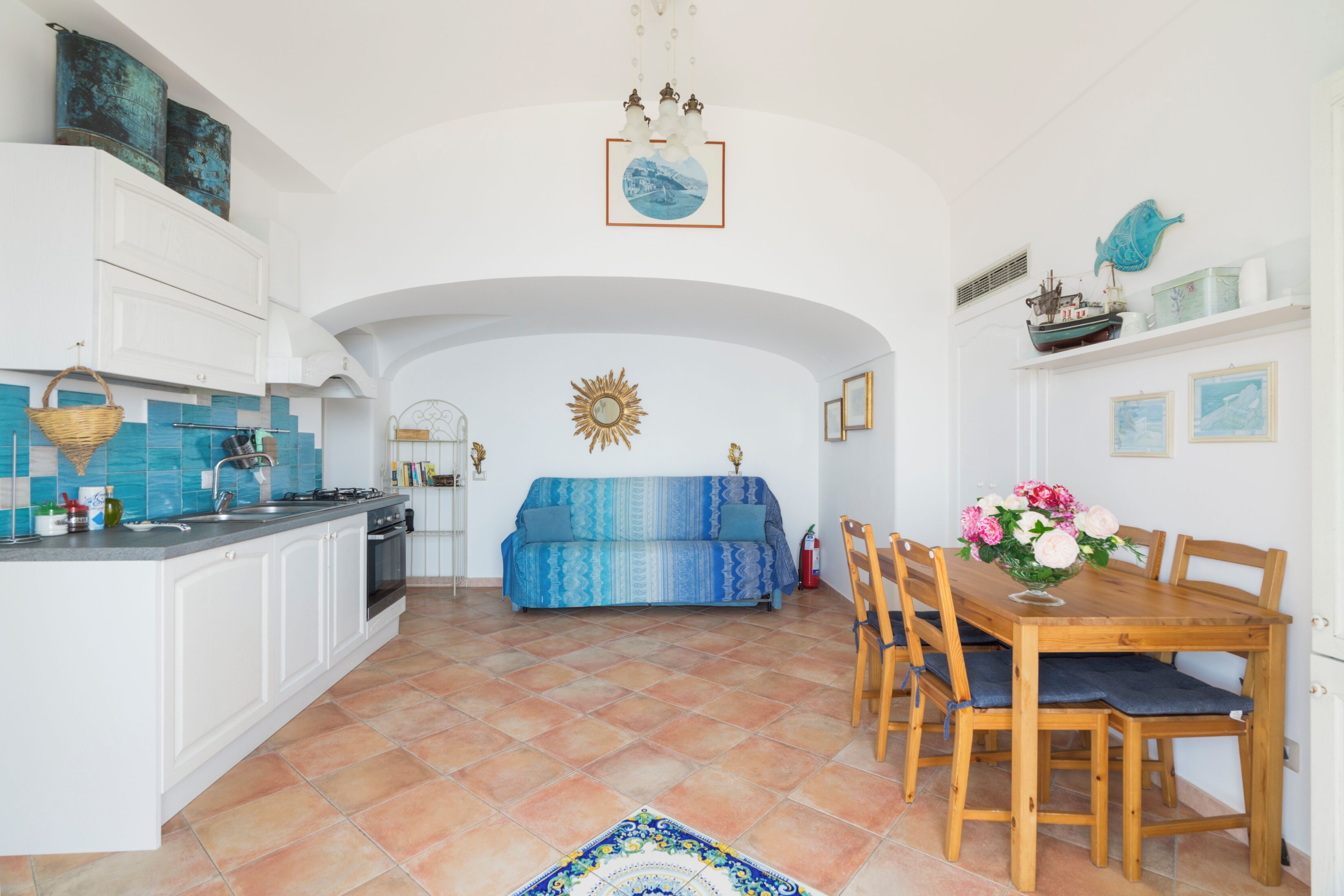A spacious kitchen with white cabinets, a dining area with a wooden table and chairs, and a blue sofa.