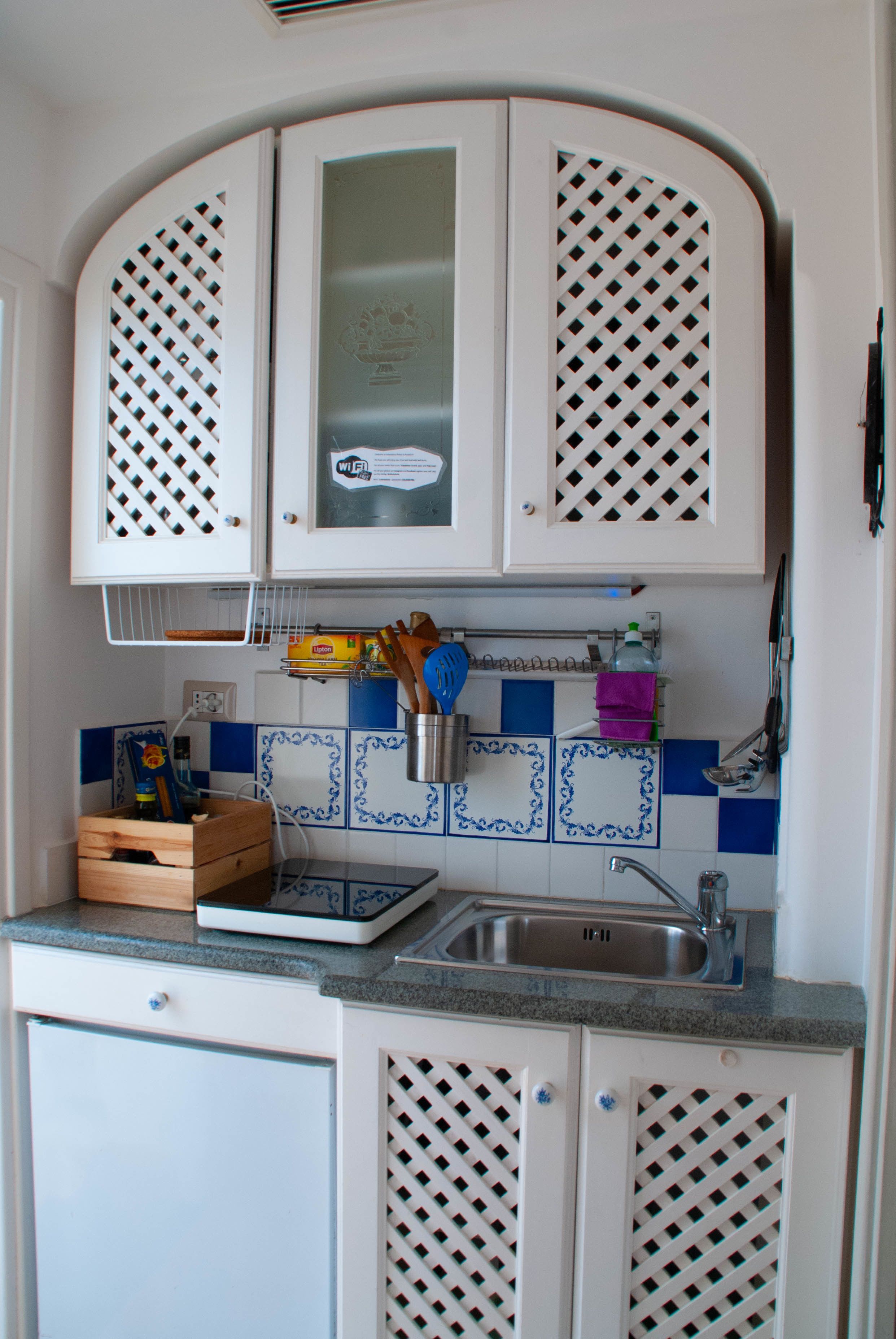 Una cocina con armarios blancos, un lavamanos de acero inoxidable y azulejos azules y blancos.