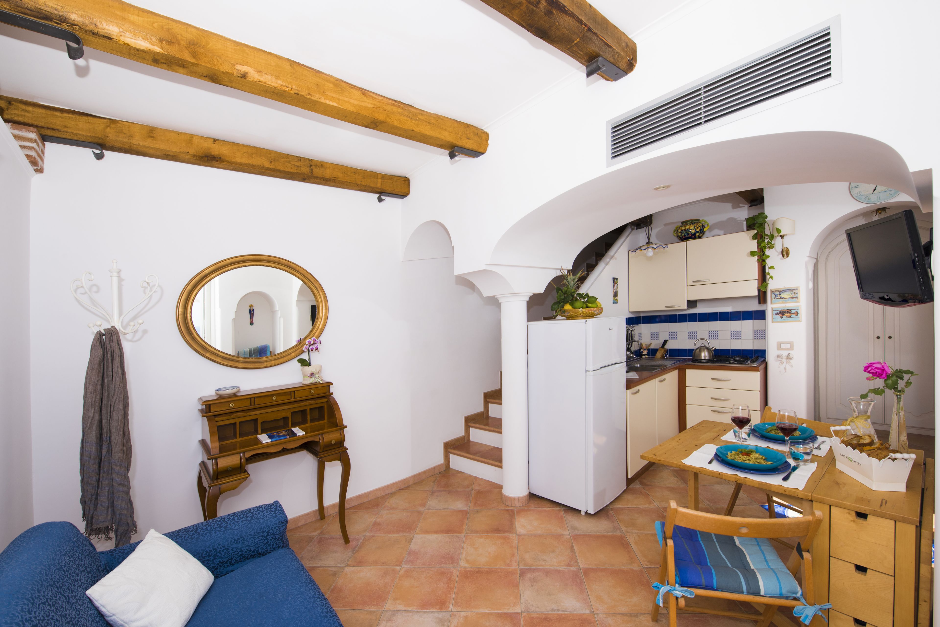Un espacio habitable compacto con kitchenette, comedor y un dormitorio con sofá azul.
