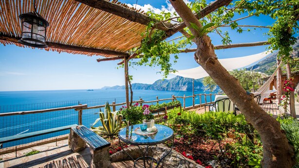 Un patio frente al mar con una mesa, sillas y un farol colgante.