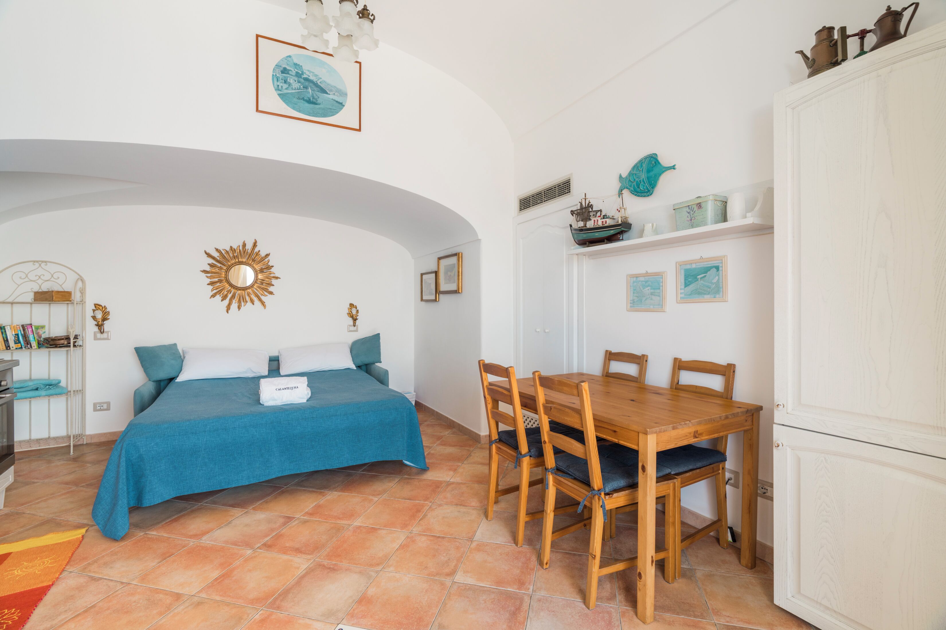 Un dormitorio con una cama, una mesa de comedor de madera, sillas, un armario blanco y una pared decorada con cuadros y objetos decorativos.