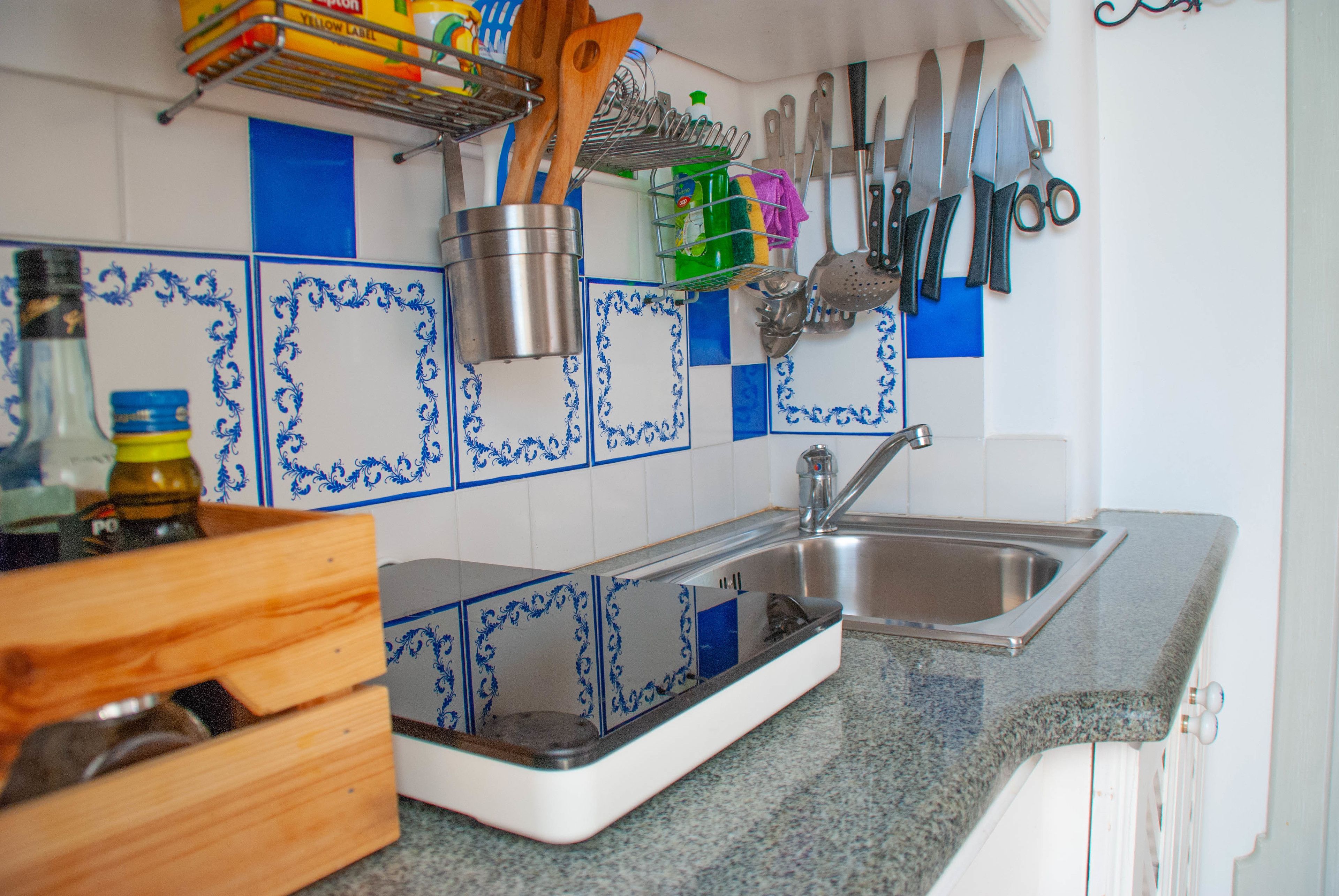 Una cocina con encimera de granito, pileta de acero inoxidable y baldosas azules y blancas con diseño.