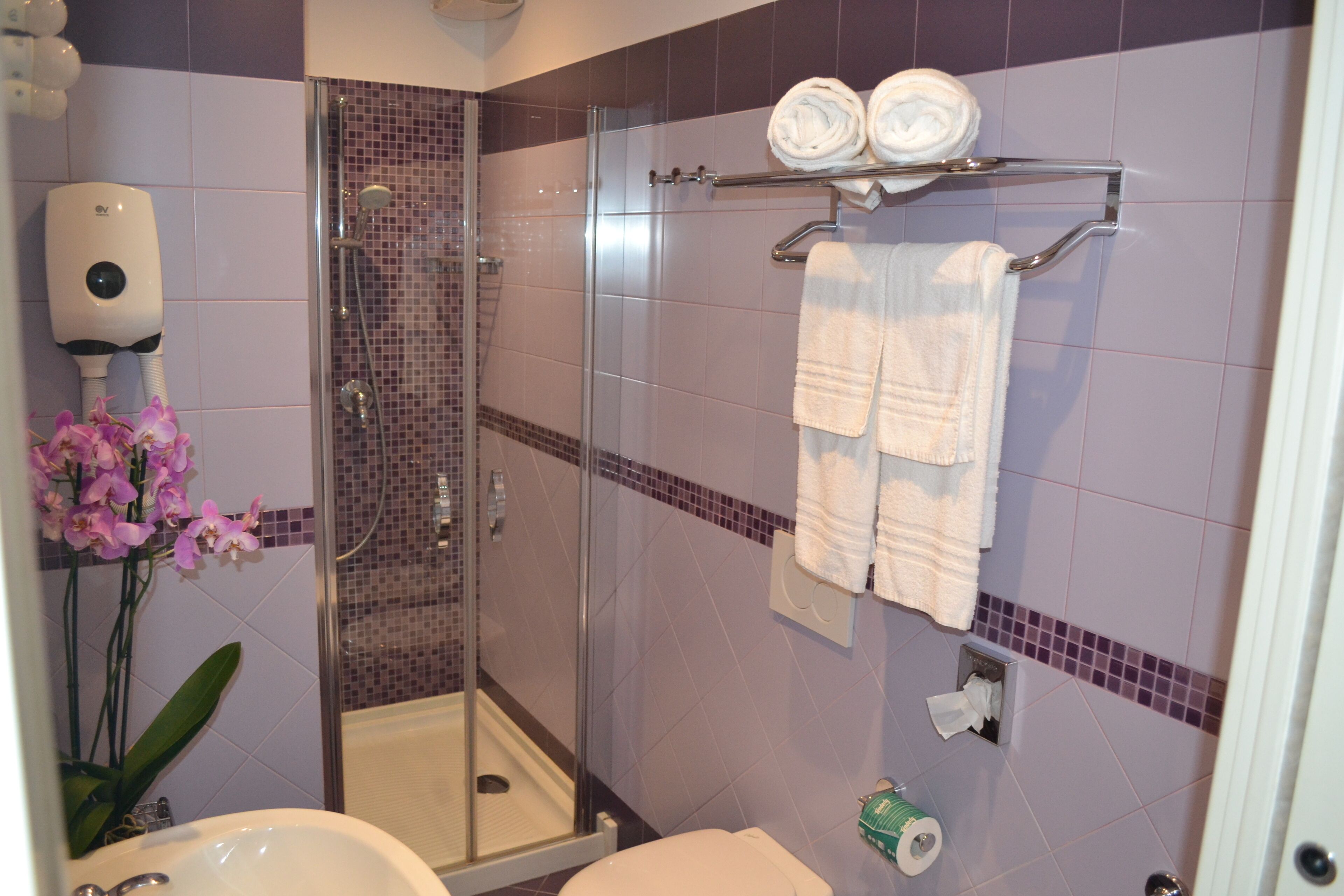 A bathroom with a glass shower enclosure, a white sink, a toilet, and a towel rack with towels.