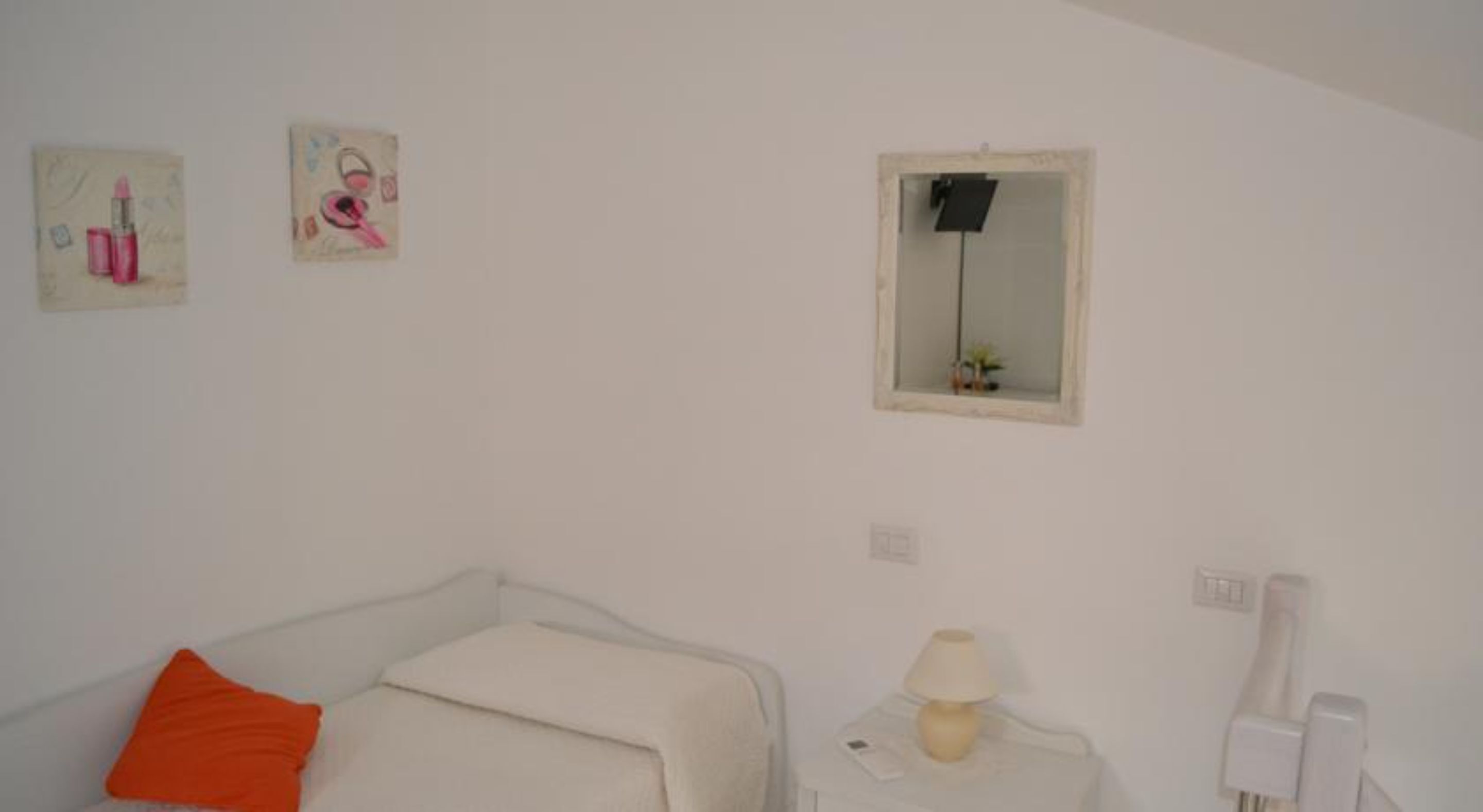 A bedroom with a bed, a bedside table with a lamp, a small mirror, and two wall-mounted pictures.