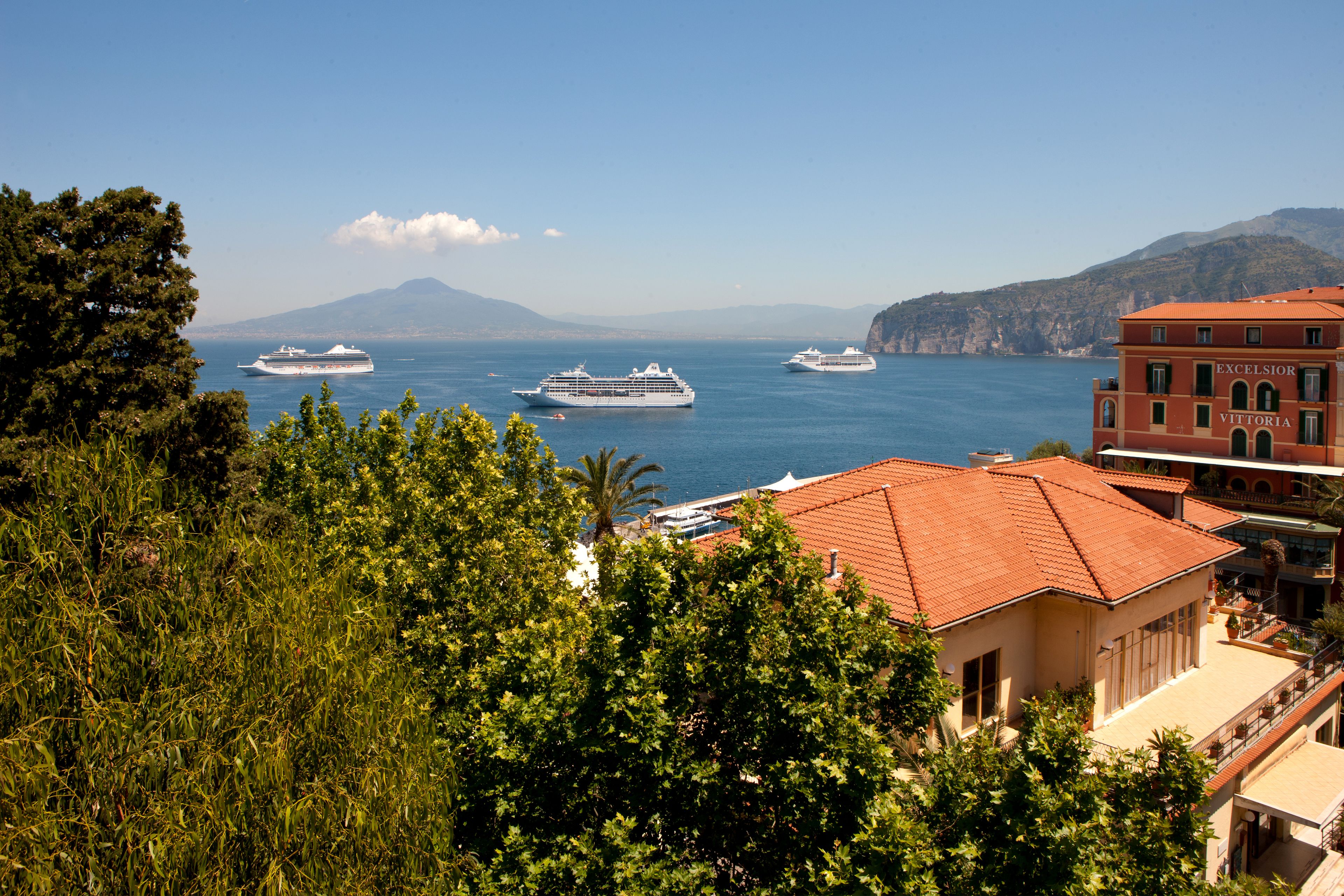 A coastal view with cruise ships and a building with "EXCELSIOR VITTORIA" signage.