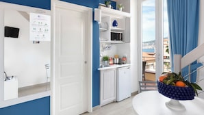 A modern kitchen with white cabinets, a built-in oven, and a sink. There is a window with blue curtains and a view of the city. - Al Centro Suites (Sorrento)