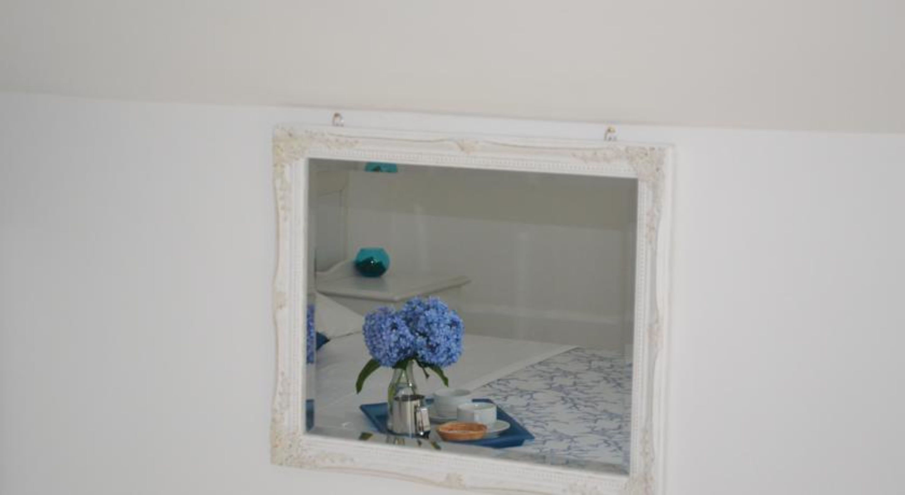 A bathroom with a white vanity, a blue vase with flowers, and a small shelf with a teal object.