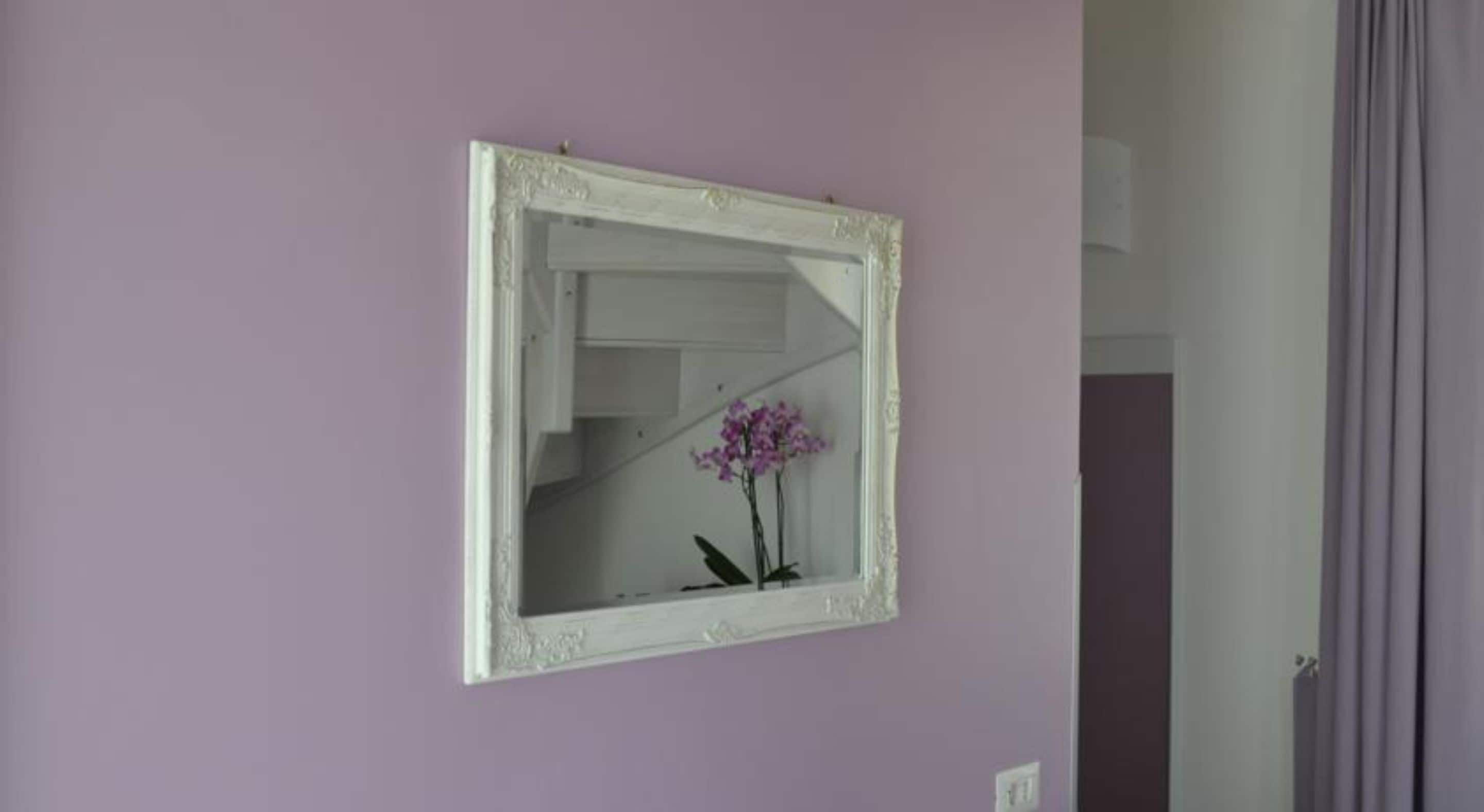 A mirror with a white frame on a purple wall.