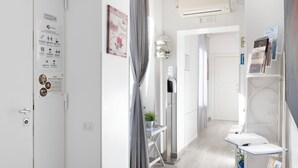 A hotel corridor with a white door, a bulletin board with notices, a small table with a plant, and a metal rack with brochures. - Al Centro Suites (Sorrento)