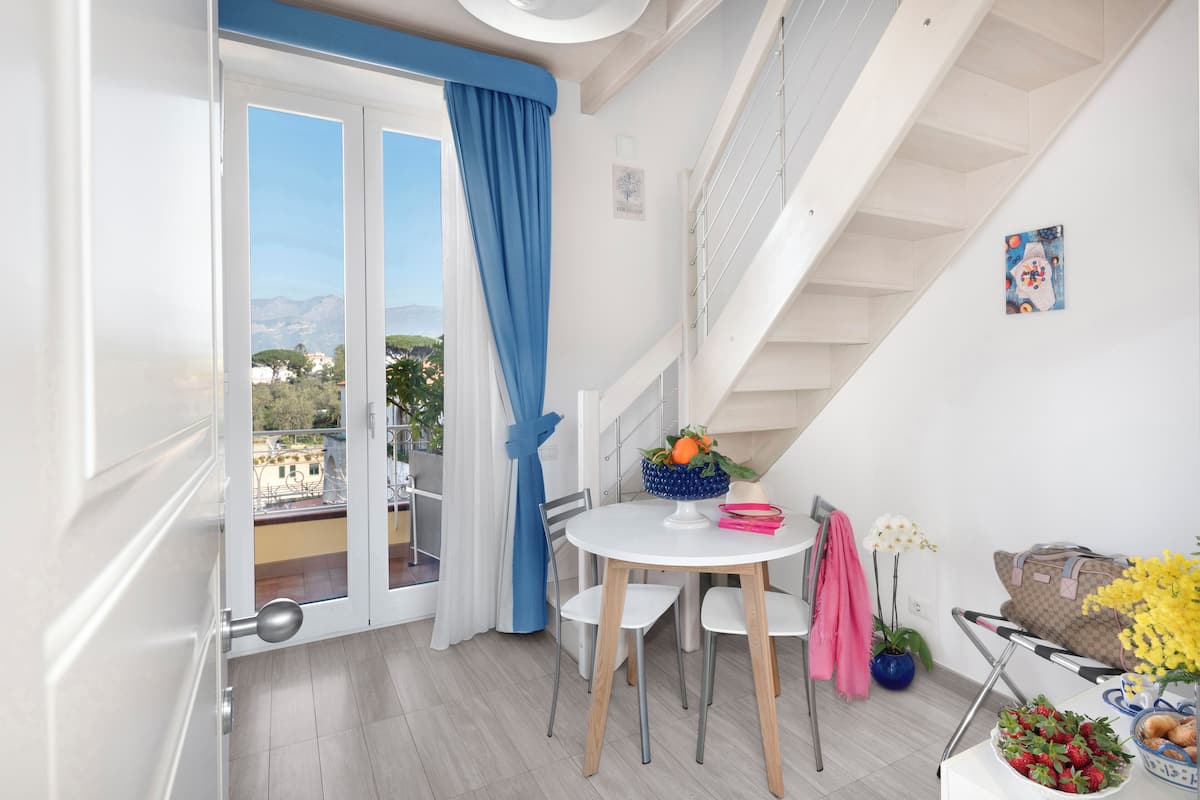 A balcony with a view of the city, a dining area with a table and chairs, and a staircase.