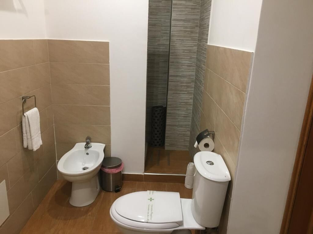A compact bathroom with a bidet, toilet, and a trash bin.