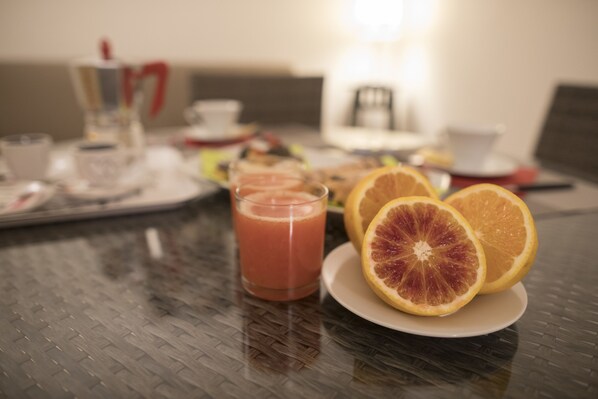 Une table de petit-déjeuner avec un verre de jus d’orange, deux moitiés d’orange et un plateau contenant divers aliments pour le petit-déjeuner.