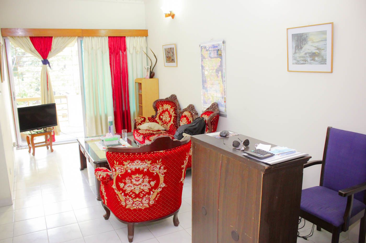 A living room with a TV, a desk, a purple chair, and a red patterned sofa.