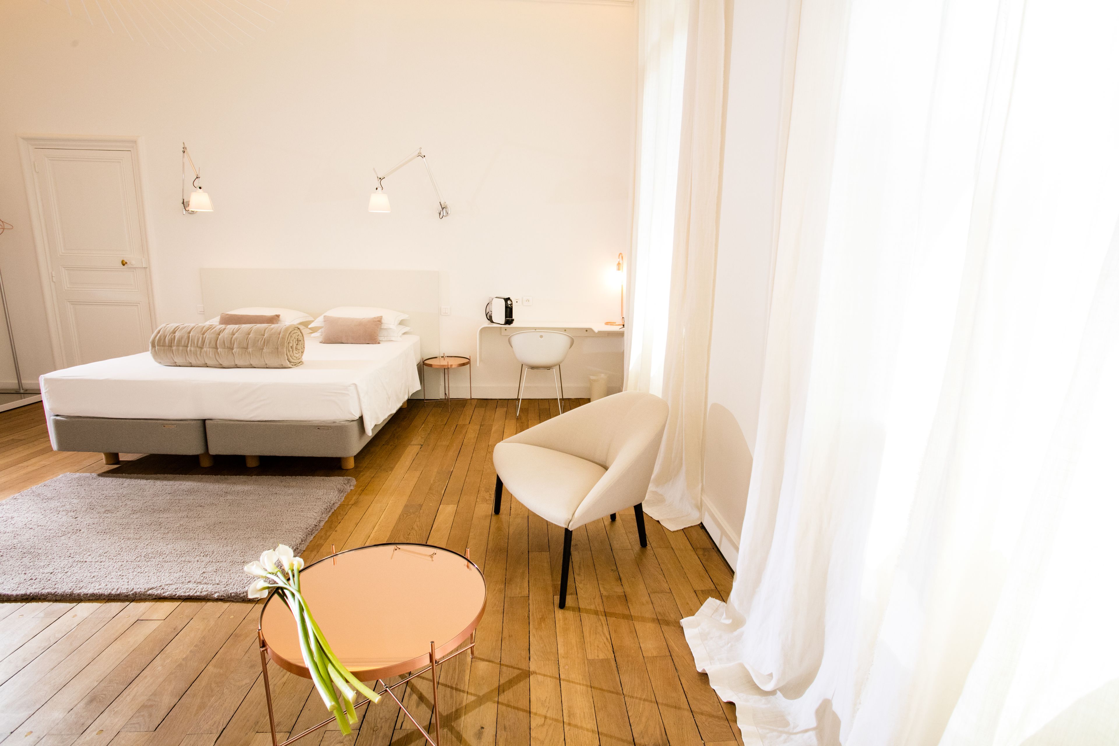 Un dormitorio con cama, mesita de noche, silla y una pequeña mesa redonda con flores.