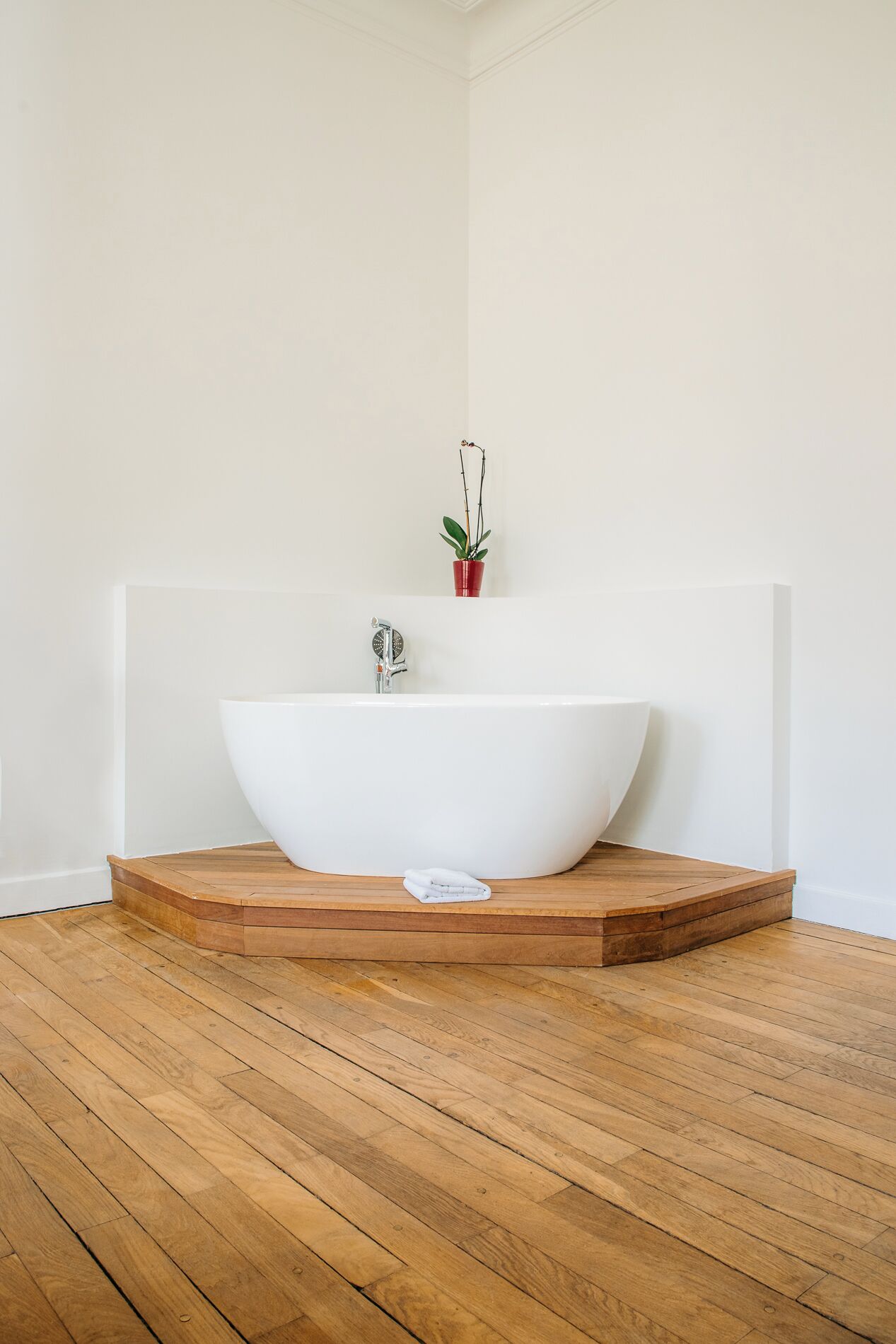 A modern bathroom with a freestanding white bathtub, a small potted plant, and a wooden platform.