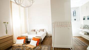 Quarto de hotel moderno com uma cama, duas cadeiras, um quadro branco e um banheiro visível por uma porta aberta.