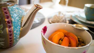A table with a teapot, a bowl of fruit, and a glass of orange juice.