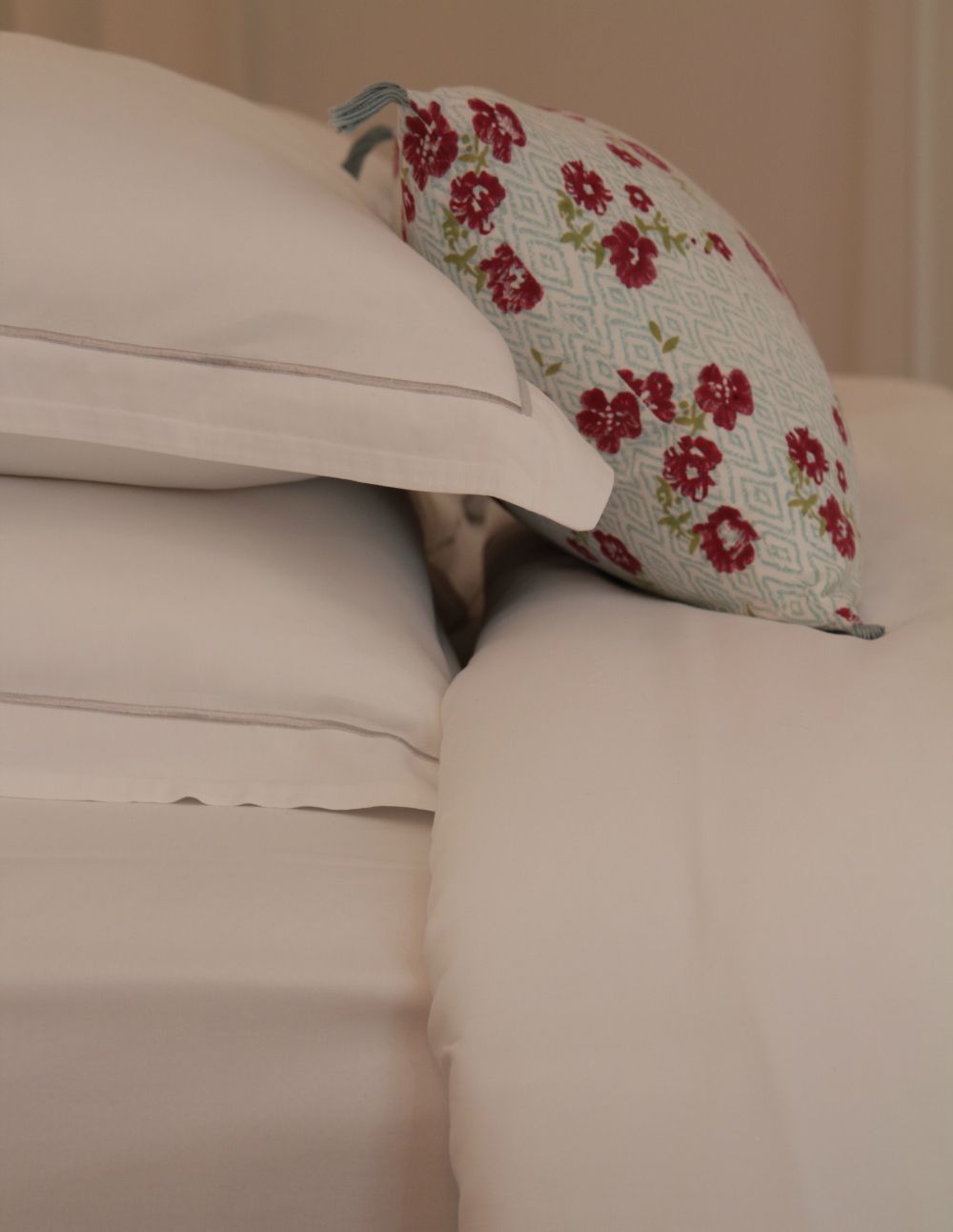 A bed with two pillows, one plain and one with a floral pattern.