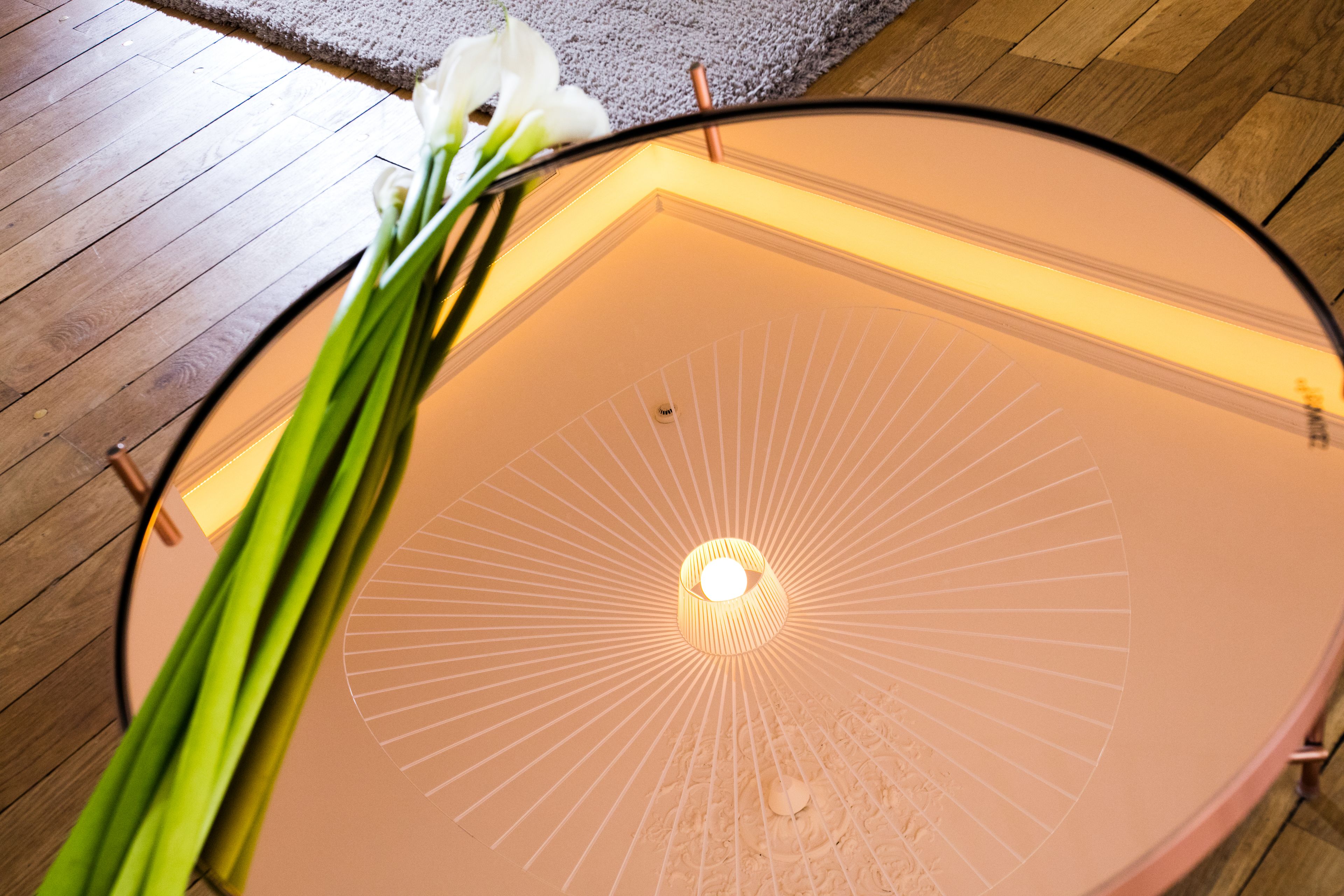 A ceiling with a radial light fixture and a vase with flowers on a wooden floor.