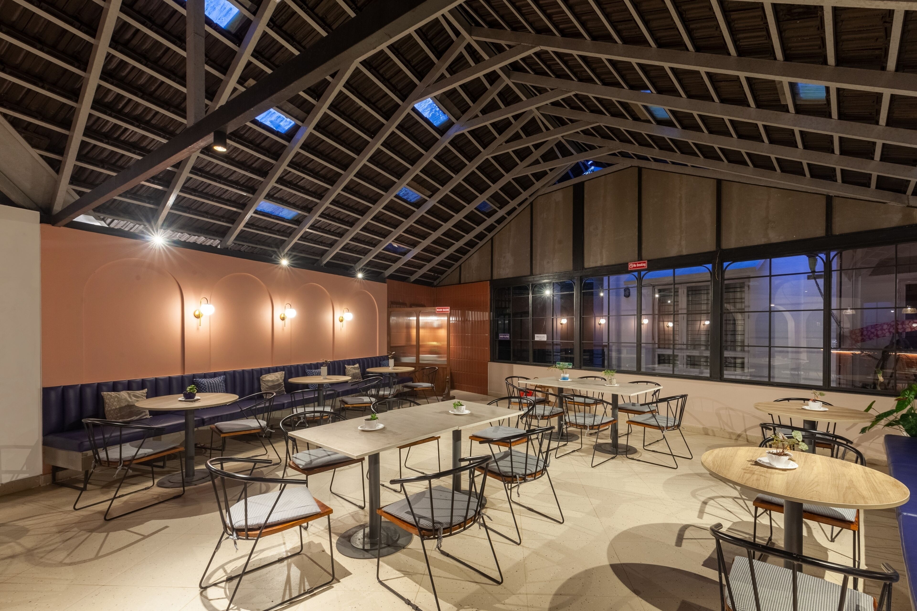 A spacious indoor dining area with high ceilings, multiple tables and chairs, and large windows providing natural light.