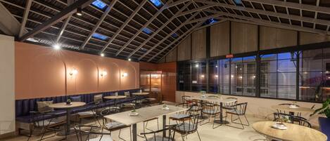 A spacious indoor dining area with high ceilings, multiple tables and chairs, and large windows providing natural light.