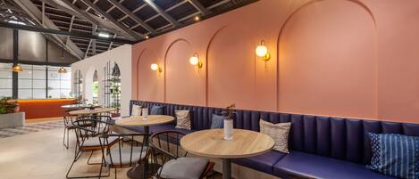 A modern cafe with round tables, cushioned seating, and pendant lighting.