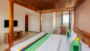 A bedroom with a wooden ceiling, a bed with a colorful bedspread, a TV on the wall, and a desk with a chair. - Treebo Vrindavan, 3 Km From Madikeri Fort (Madikeri)