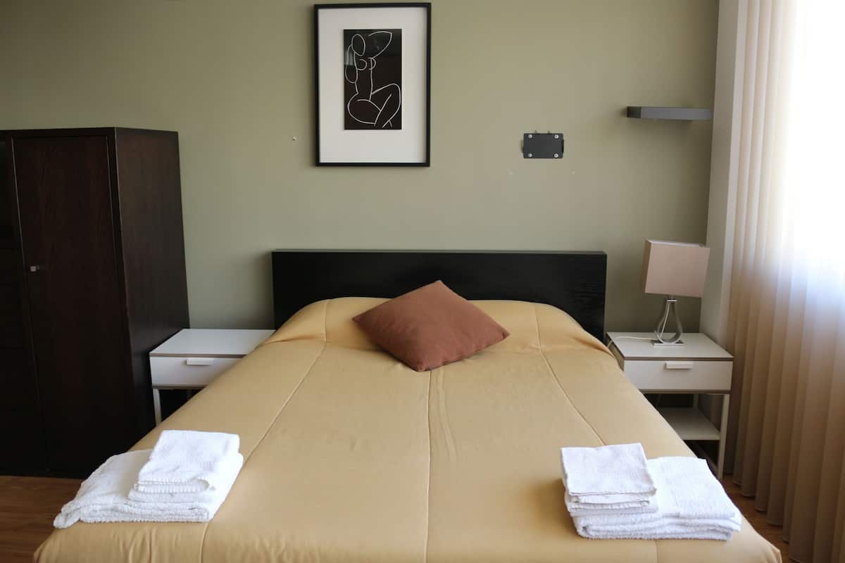 Habitación de hotel con cama, mesita de noche, lámpara, un cuadro en la pared y un armario.