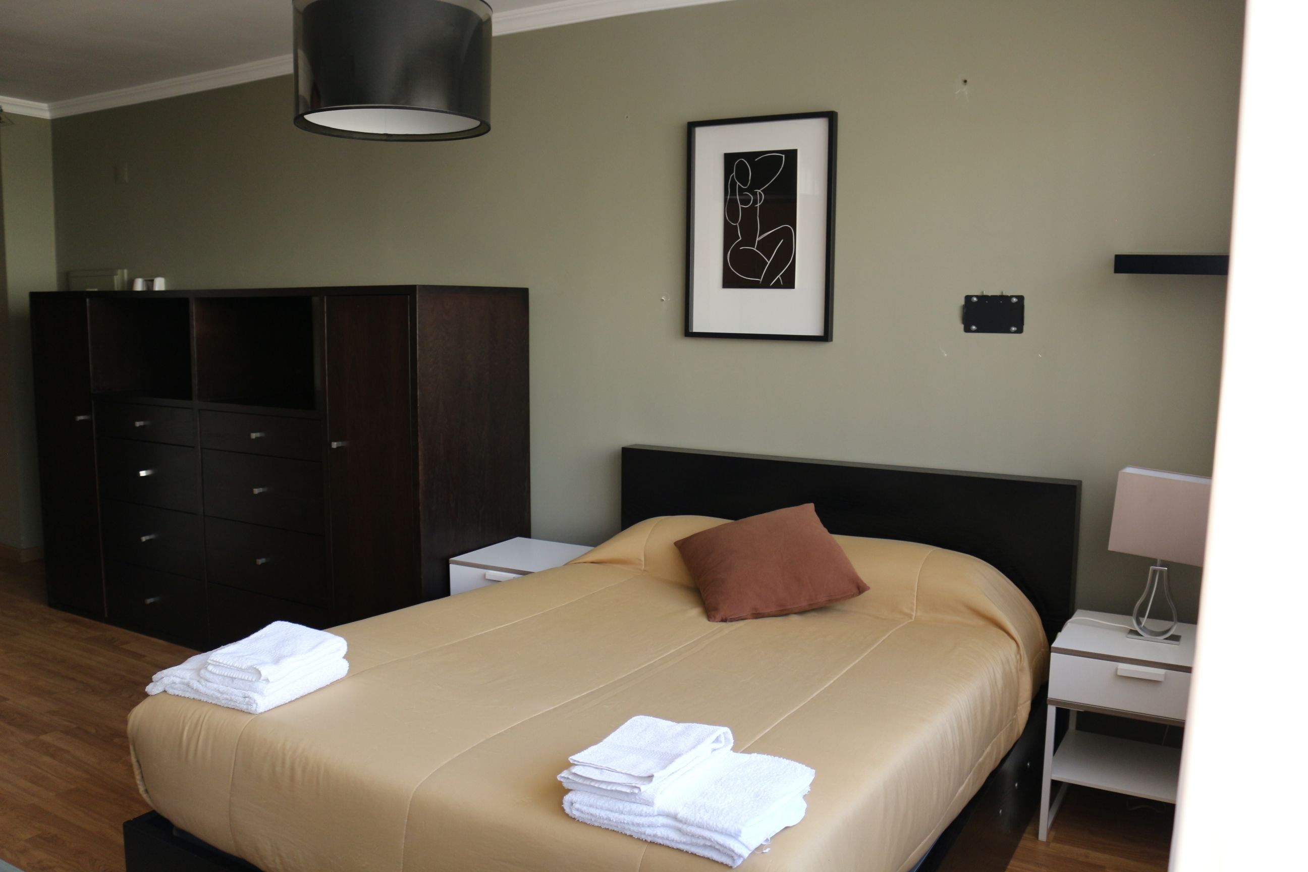 A hotel room with a bed, a wardrobe, a bedside table with a lamp, and a framed artwork on the wall.
