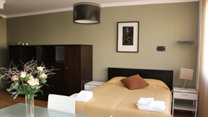 A hotel room with a bed, a nightstand, a table with a vase of flowers, a framed picture on the wall, and a wardrobe. - Studios Porto Solar (Porto)