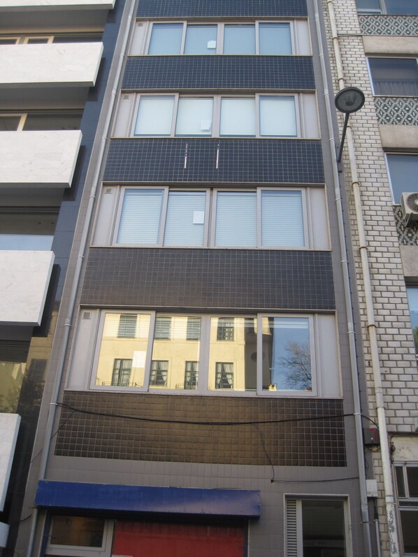 A multi-story building with a mix of window styles and a visible red awning at the ground level.