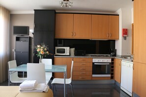 A compact kitchen with wooden cabinets, a microwave, a stove, and a dishwasher. There is a dining table with chairs and a vase of flowers. - Studios Porto Solar (Porto)