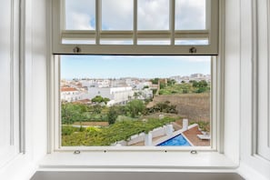 A window view of a residential area with a swimming pool, white buildings, and greenery. - Casa Mãe Lagos (Lagos)
