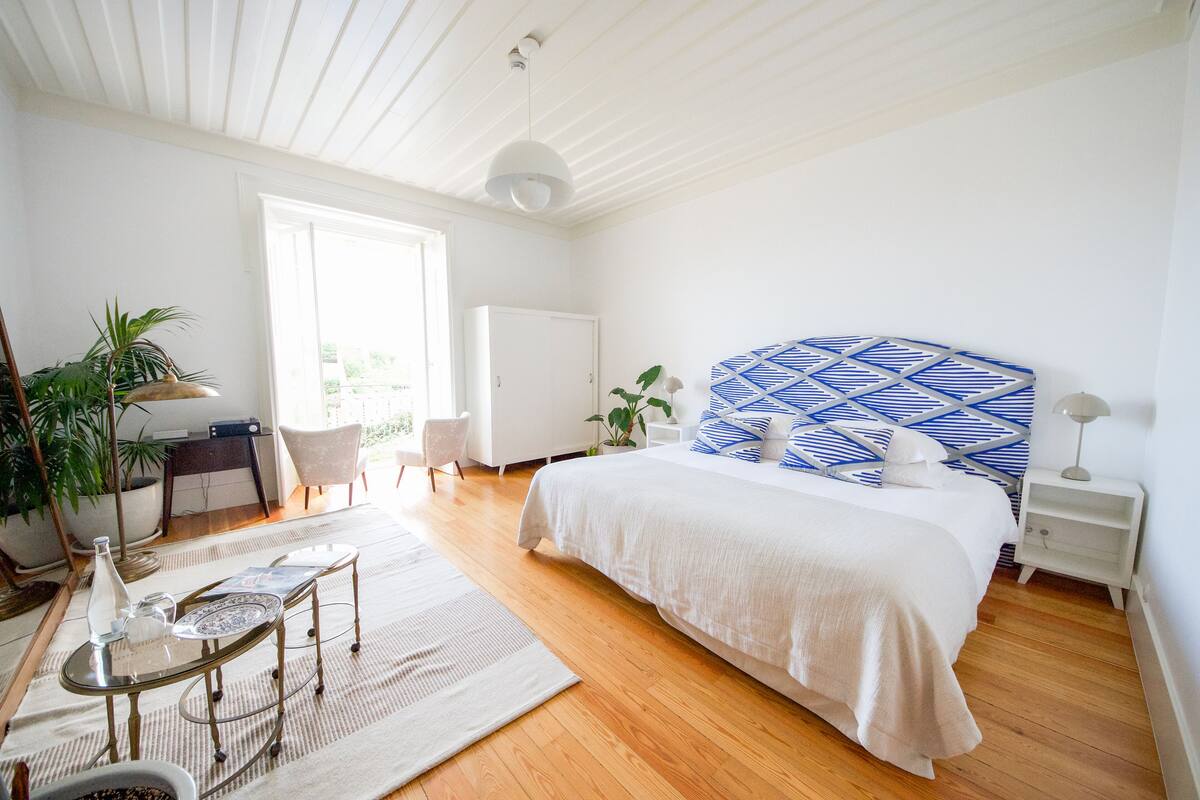 Quarto com uma cama grande, uma escrivaninha, uma cadeira e um vaso de planta.