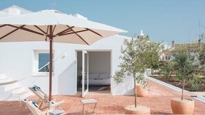 Terraza en la azotea con una sombrilla blanca, sillones de descanso y plantas en macetas.