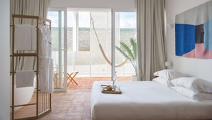 Habitación de hotel con cama, perchero, bandeja con frutas y vistas al exterior.