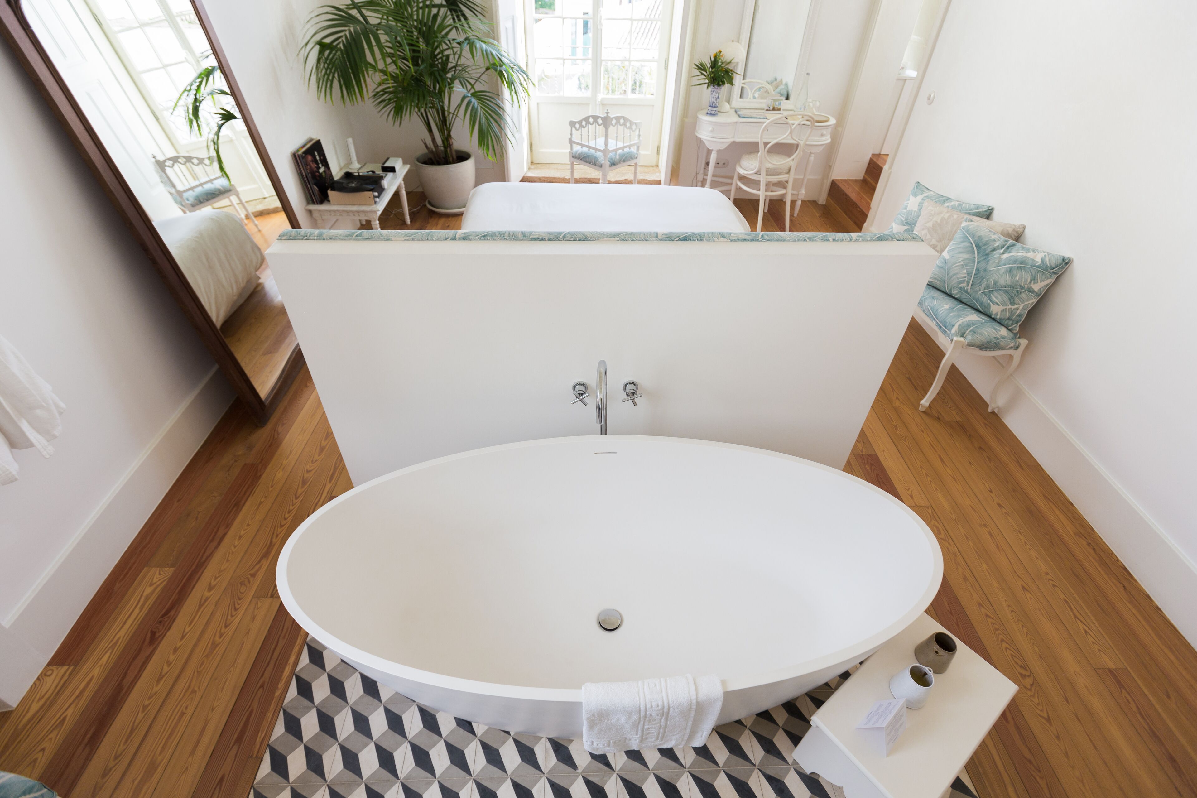 A modern bathroom with a freestanding bathtub, a small table with toiletries, and a potted plant.