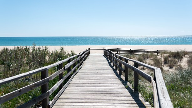 Una pasarela de madera que conduce a una playa con cielos despejados.