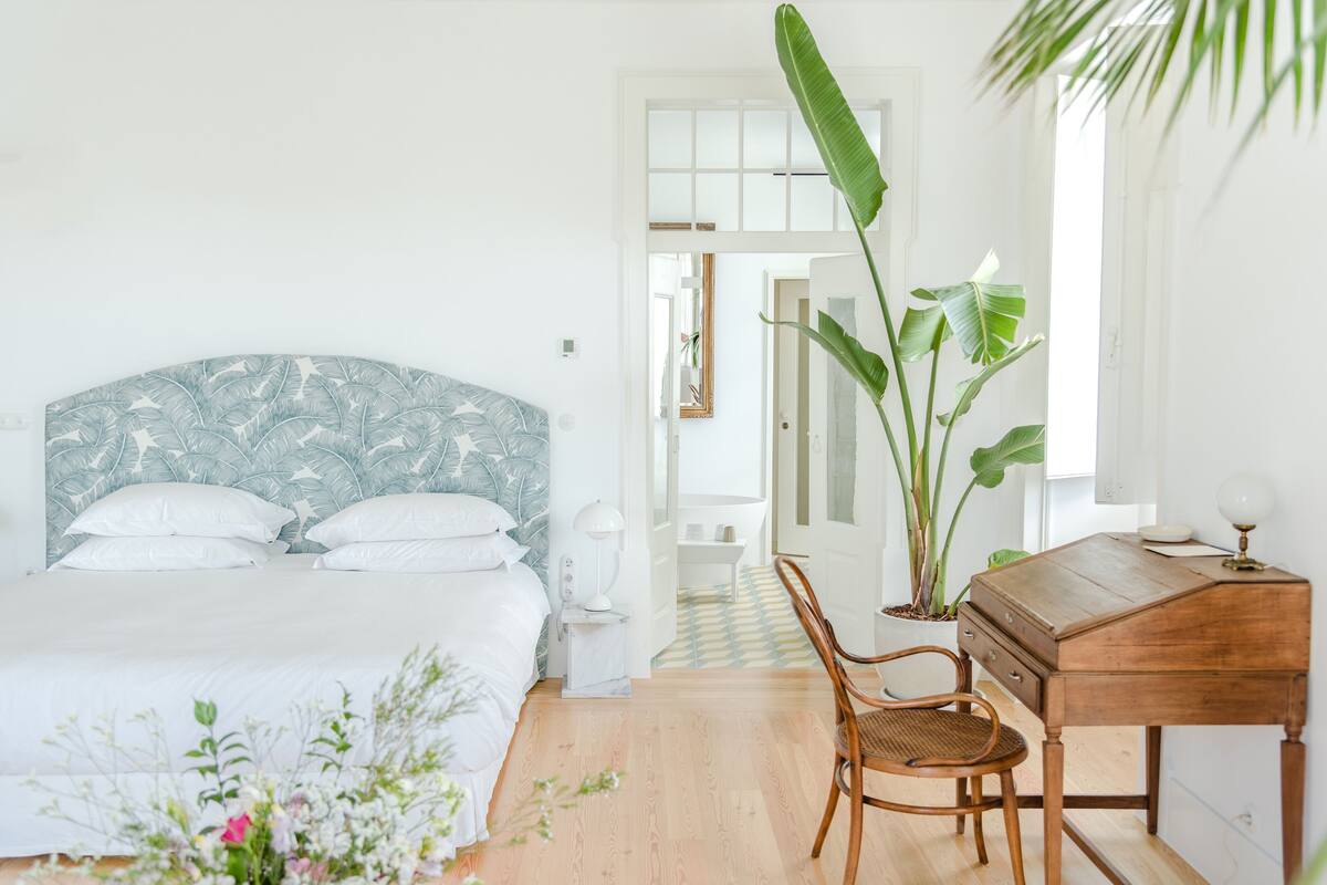 Quarto com cama, escrivaninha, cadeira e planta em vaso.